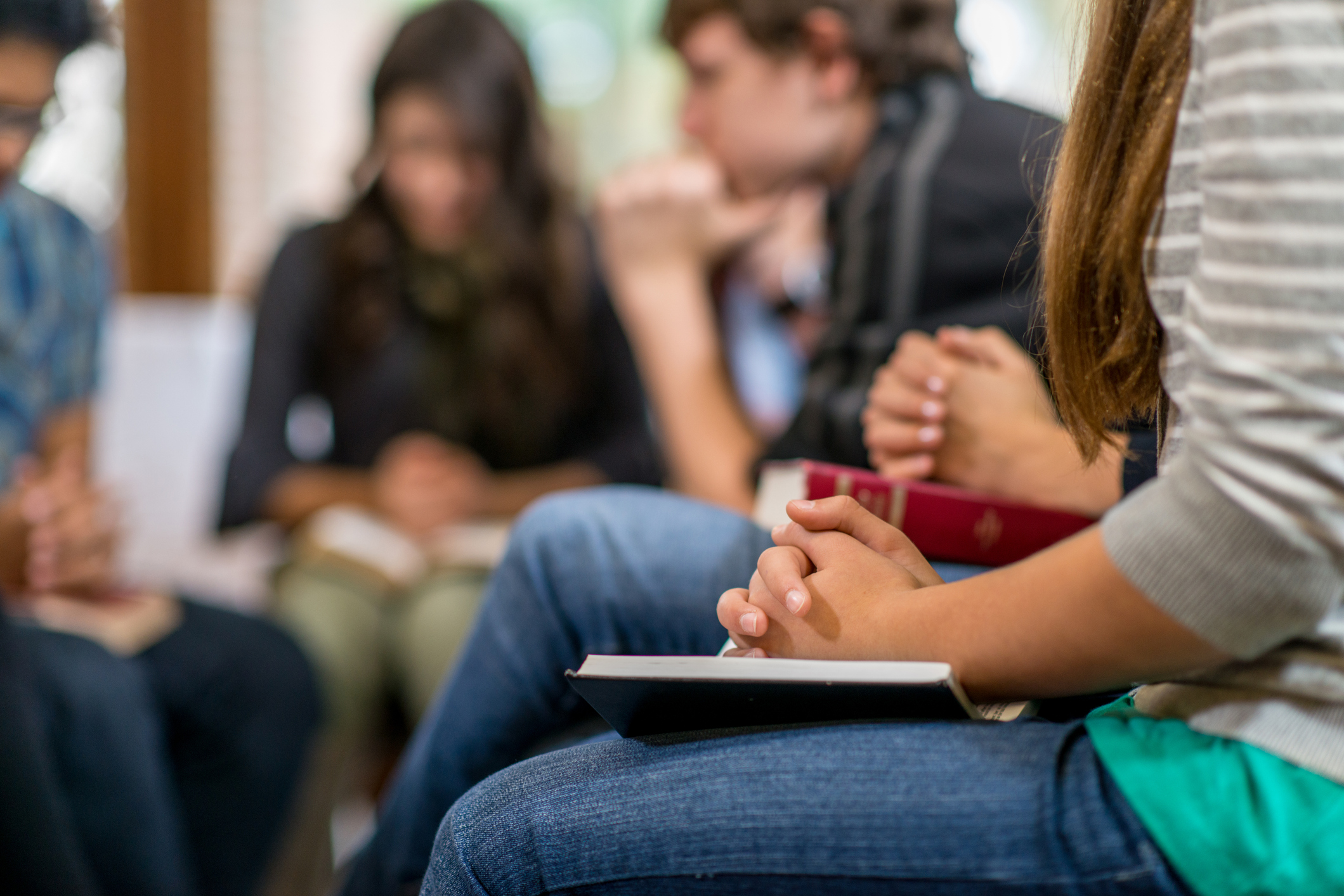 A group of people sitting in a circle praying and discussing scripture with Bibles in hand during a Valley Church Community Group meeting, illustrating how small groups strengthen faith and relationships.